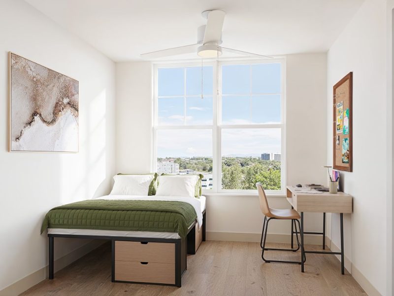 Furnished bedroom rendering in a modern Brickside apartment, featuring a bed, desk, chair, and window with natural light.